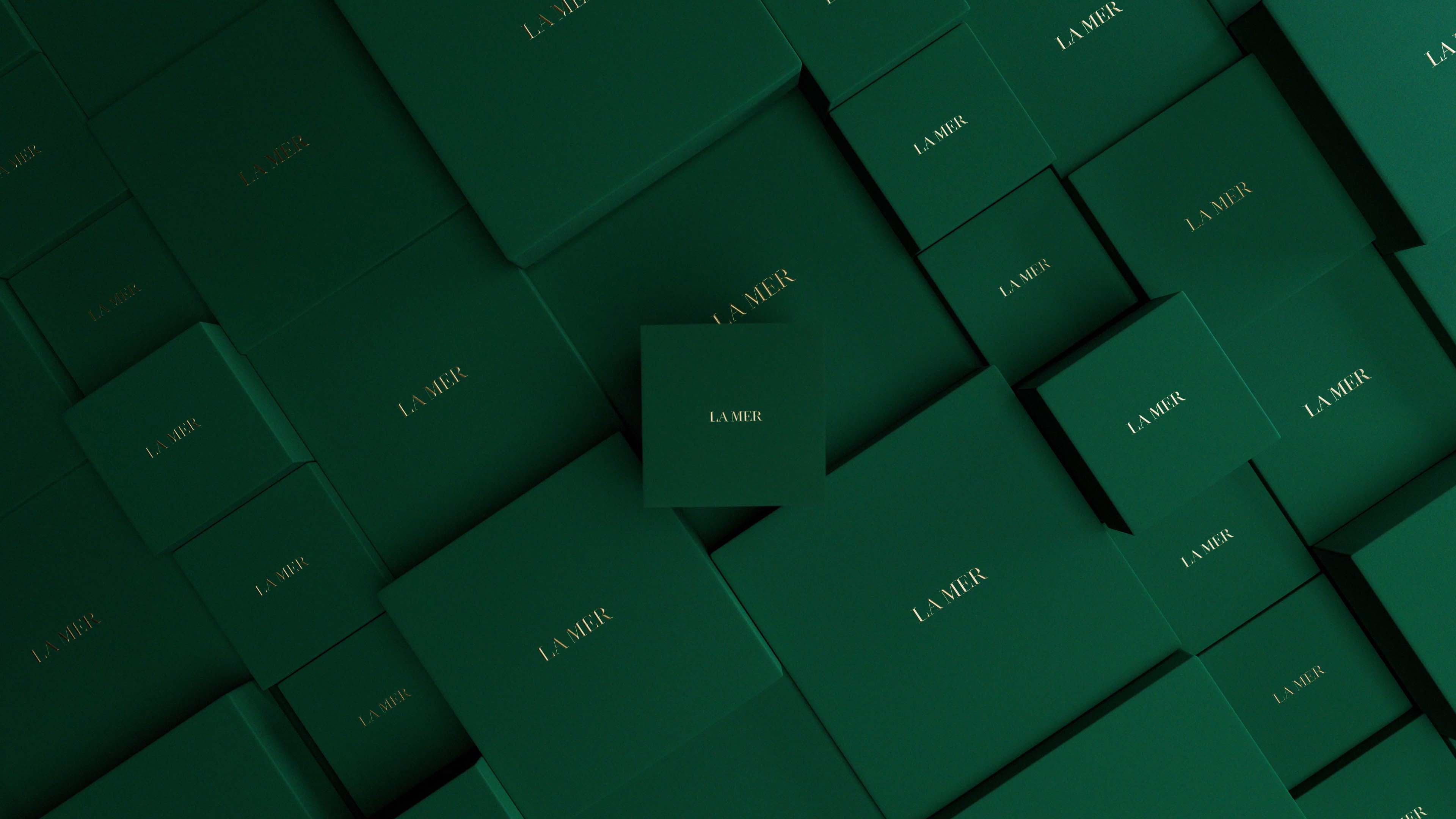 Image of multiple green la mer gift boxes laid out on an angle and one la mer box straight on in view.